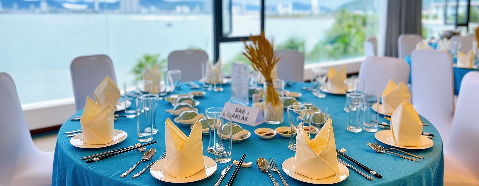 A close up shot of a round table covered in a blue cloth with neatly founded napkins on plates - Alibu Resort