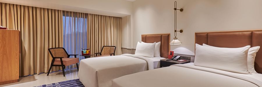 A hotel room with two twin beds, a colorful rug, a dresser, and a view through a window with curtains - The Dukes Retreat
