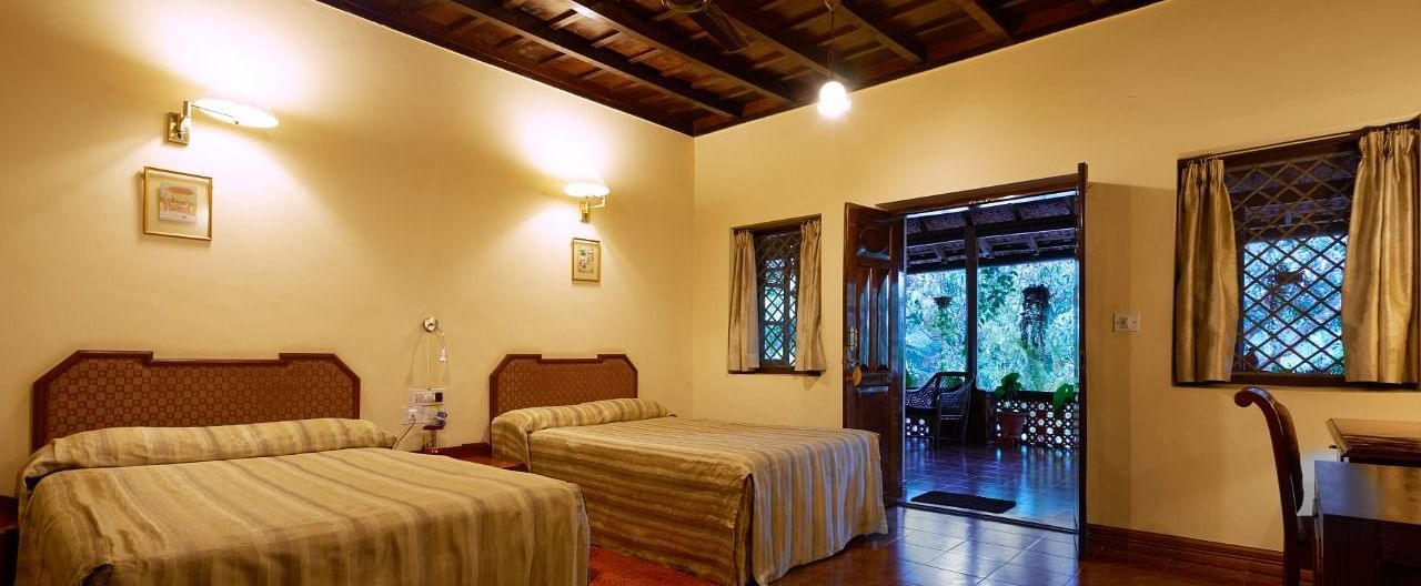 Spacious room with twin beds, wooden ceiling beams, and windows showing greenery - BluSalzz Collection - Tranquil Resort, Wayanad