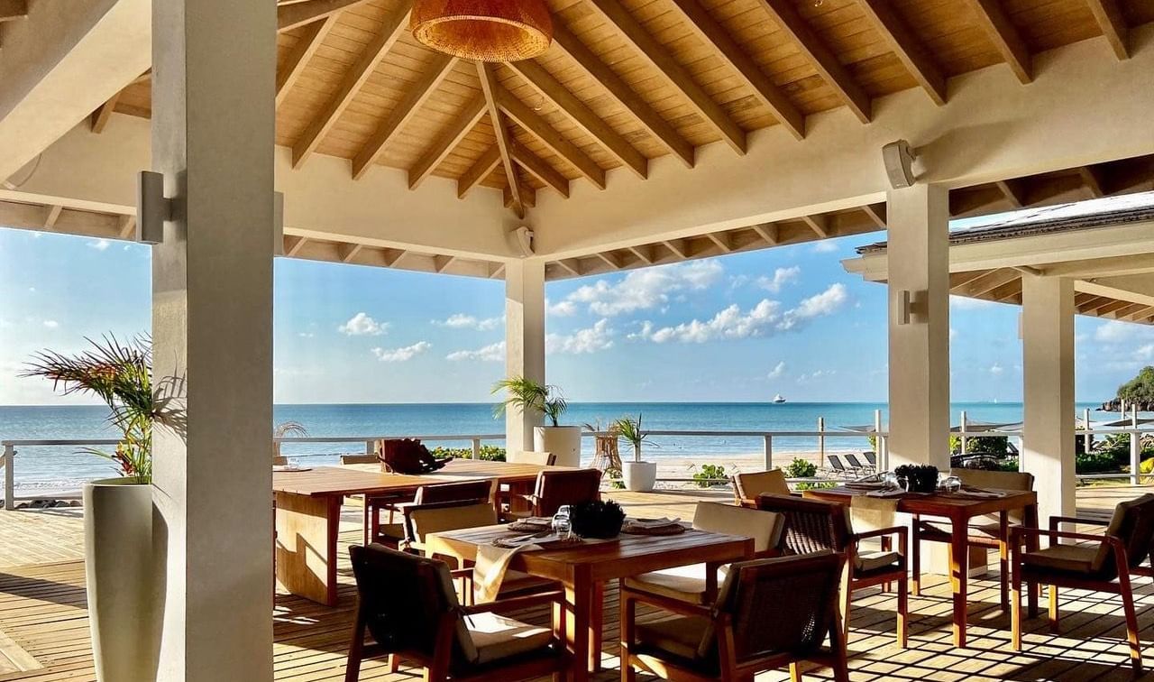 Open-air beachfront restaurant with wooden furniture and ocean views, under a high thatched roof ceiling at Tamrind Hill Resort and Villas
