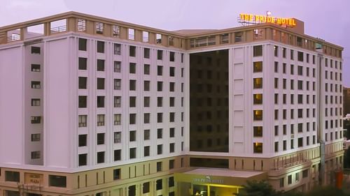 Facade of Pride Plaza Ahmedabad hotel with its name lit up atop the building, set against a glowing sunset sky for a striking evening view