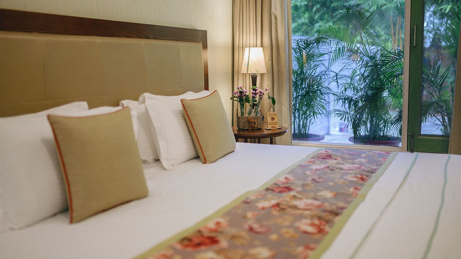 A double bed with white pillows, beige headboard, and a view of greenery through the glass door at Karma Chalets.