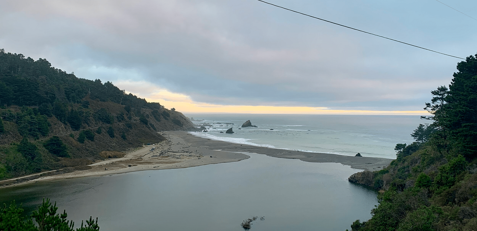 A river flows into the ocean under an overcast sky, with a shoreline visible in the distance.