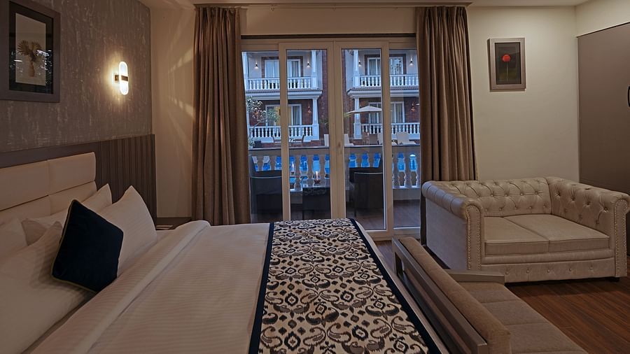 Sideview of the bedroom with comy sofa nd bed and large window with green view at Grand Continent, Anjuna - A Sarovar Portico Affiliate Hotel  