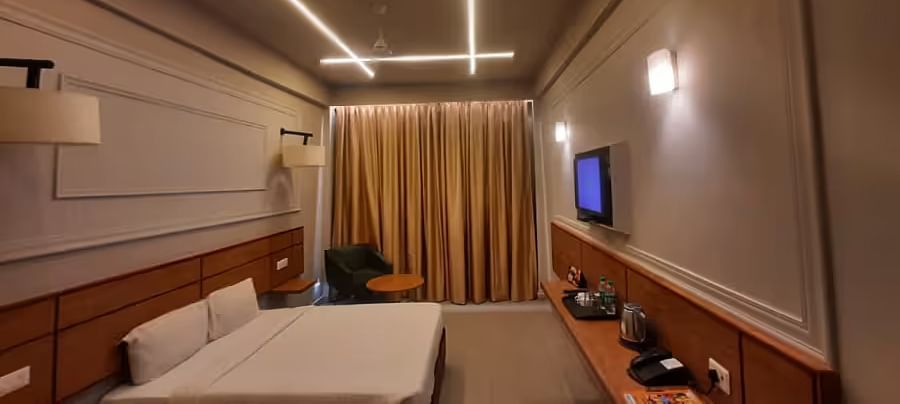 View of a modern hotel room with ambient lighting, a comfortable bed, and a wall-mounted TV - Max Hotel Prayagraj.