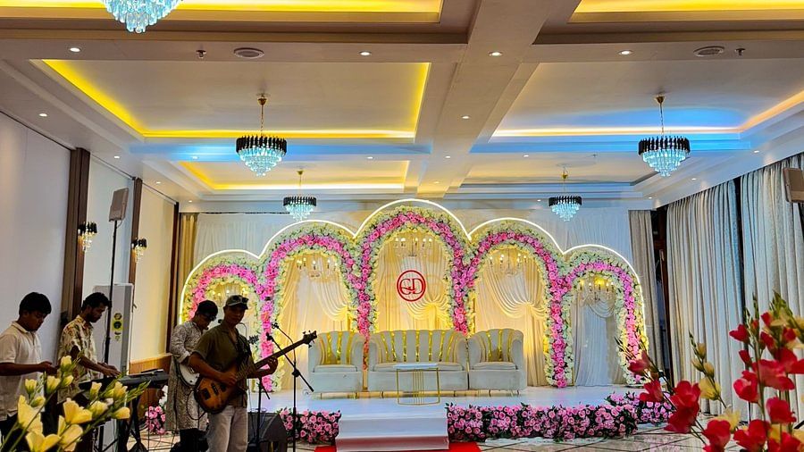 An event hall at Silver Sand Sea Princess Beach Resort, Port Blair, with a stage featuring floral arches and musicians performing.