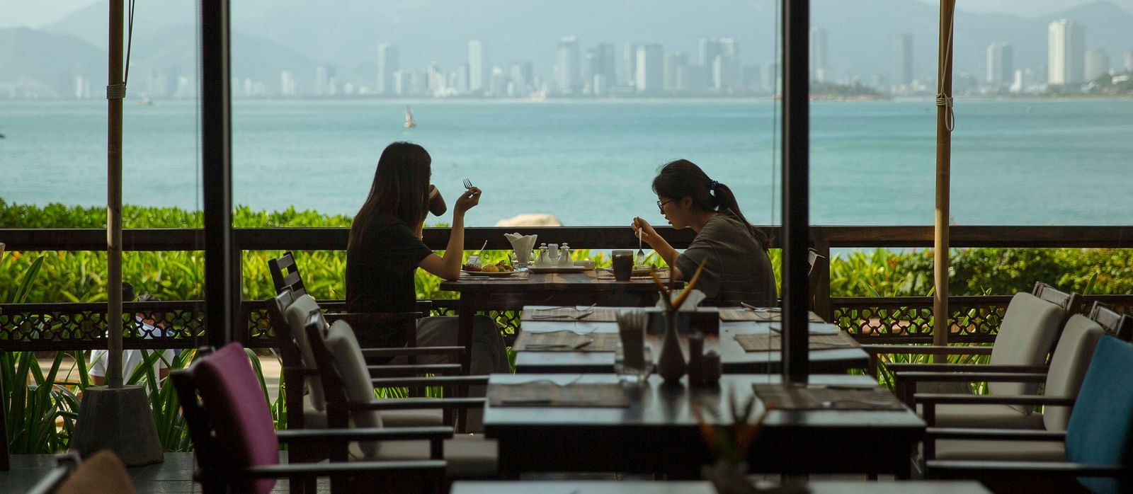 Two women dining with a coastal city view in the background - Alibu Resort Nha Trang