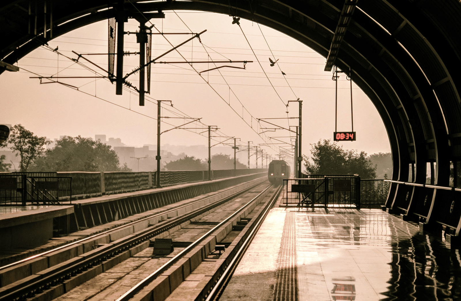 A metro station with a train approaching towards the platform on an evening.