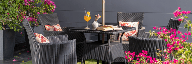 Outdoor patio space at The Atara, Gurugramis set with a dining table and chairs beneath a light-colored umbrella, surrounded by bright, blooming flowers and green foliage