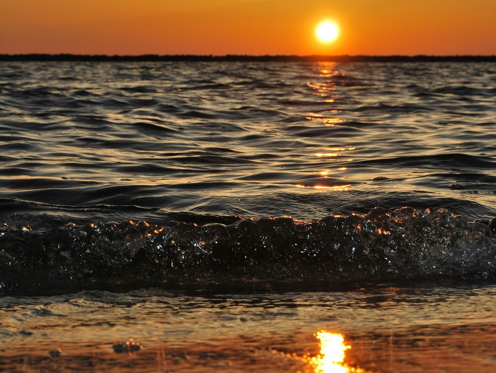 a wave of water hitting the shore of a beach during golden hour