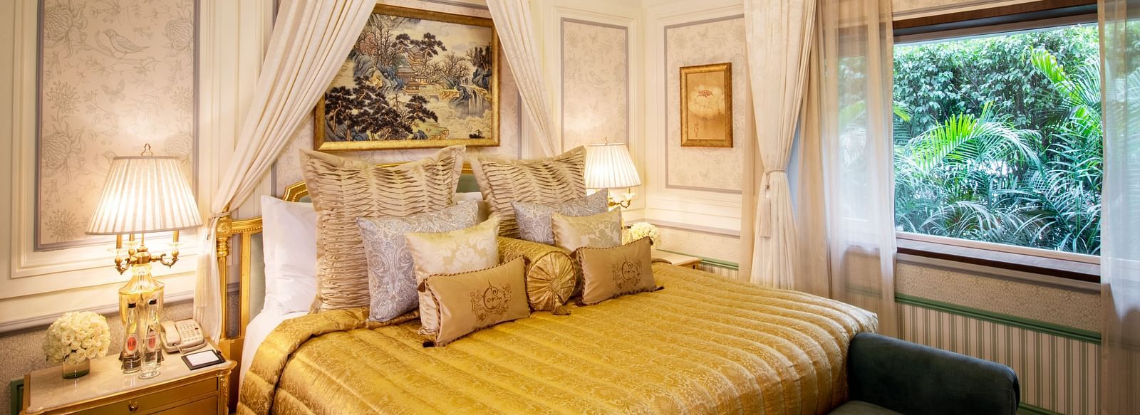 Image of a luxurious bedroom with a golden comforter, neatly arranged pillows, and cushions - The Claridges New Delhi