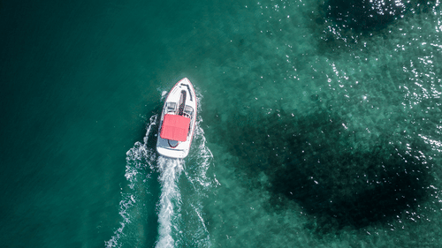 An aerial shot of a boat moving through waters leaving a trail behind it.
