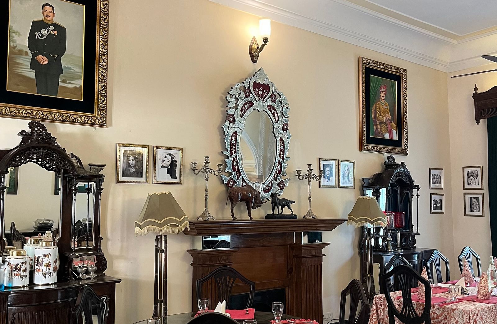  A room with traditional decor, featuring a ceiling fan, framed portraits, and dining tables - Khas Bagh, Jaipur.