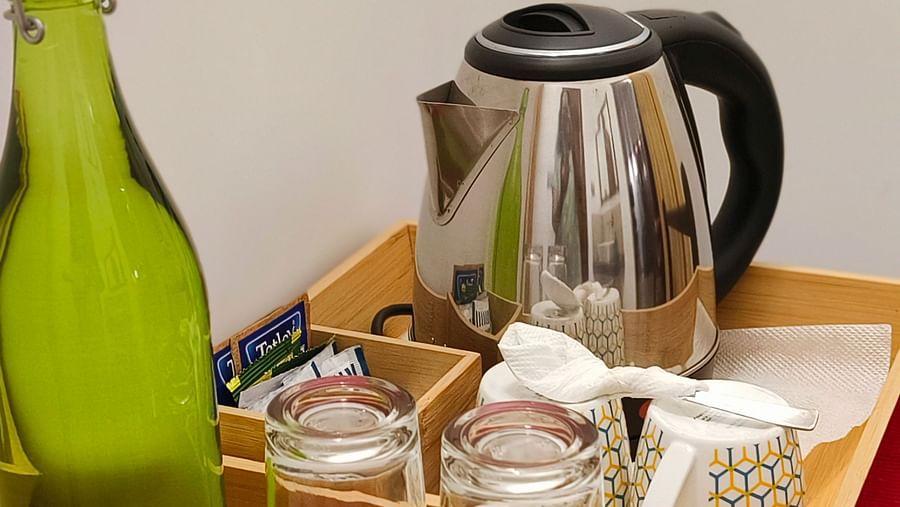 A tea and a coffee maker kept in a tray with cups and a green water bottle in 103 room at Ananda Holiday Home, Wayanad 1