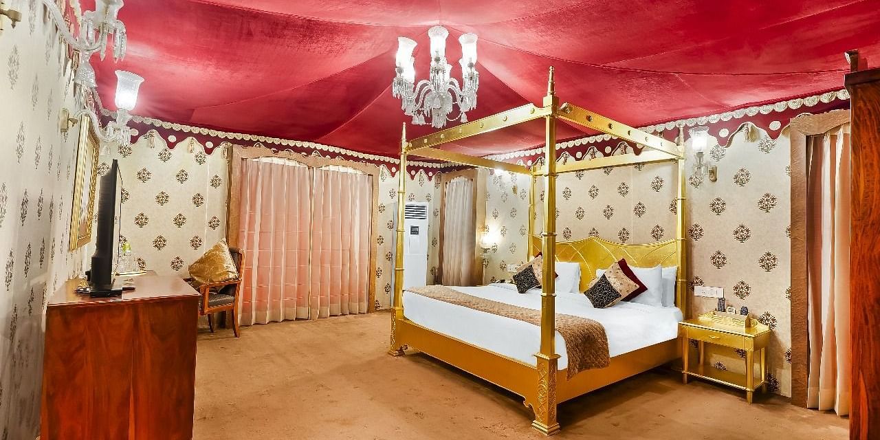 A lavishly decorated tent suite at the Rajasthali Resort & Spa in Jaipur features a four-poster bed, ornate furnishings, and a red draped ceiling.