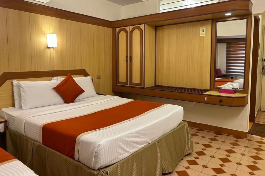 Single occupancy room at Hotel Swagath, Bangalore with a cozy bed, wooden wardrobe, and bedside lamp.