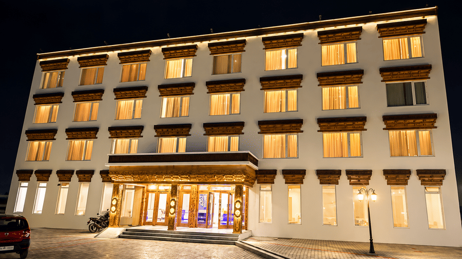 Hotel building exterior at night with illuminated windows, a lit-up carved wooden entrance canopy and a driveway with parked cars nearby.