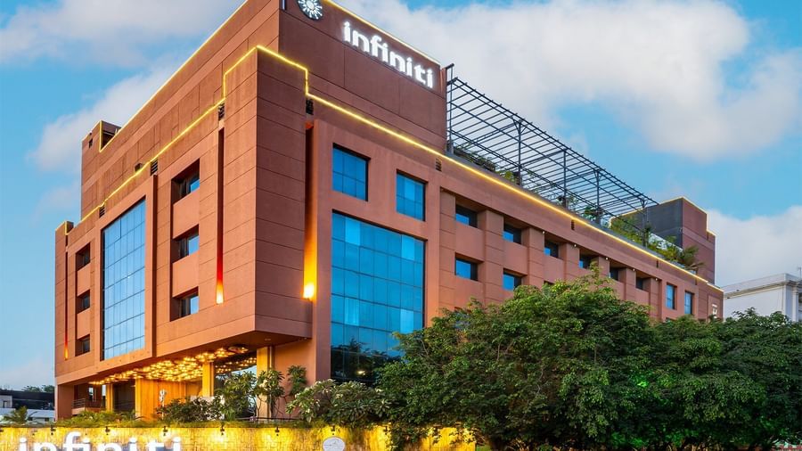 Exterior view of a multi-storey Infiniti Hotel, Indore with large glass windows, landscaped greenery, and visible signage on the top.