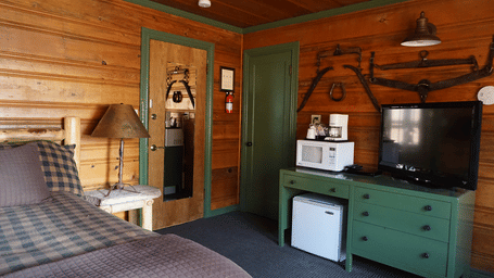 One of our Shaver Lake rooms featuring a double bed, a lamp on a night stand, a green cabinet and wooden paneling throughout.