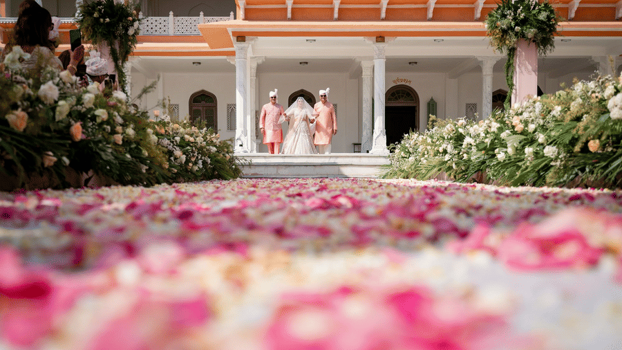 Bride walking down a petal-strewn aisle towards a grand palace entranceat  Fateh Vilas Collection Udaipur