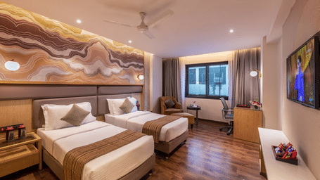 A Club Twin Room at Lords Plaza Surat with 2 single beds, an upholstered headboard, wall art, a ceiling fan, and a seating space near the window.