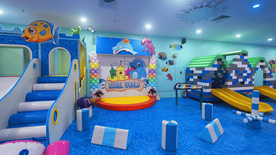 A small performance stage with a cartoon backdrop sits between 2 large slide structures at Tic Tac Tot.