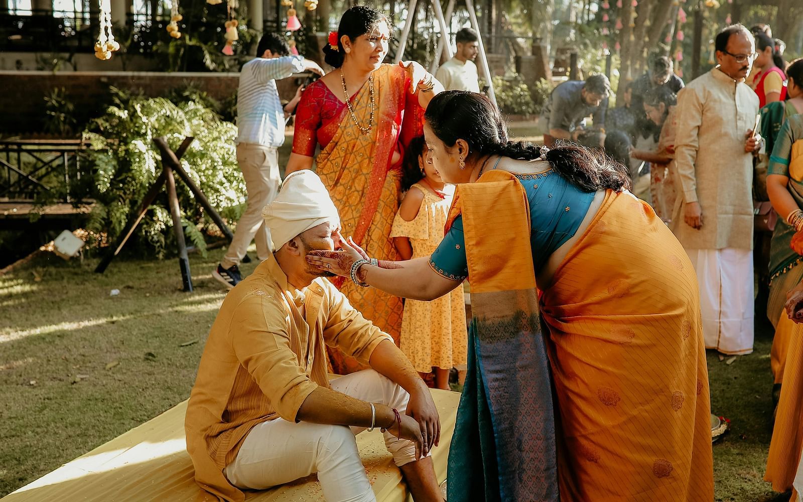 The Indian wedding ritual of haldi being performed in a lawn where a woman is applying turmeric on the groom.