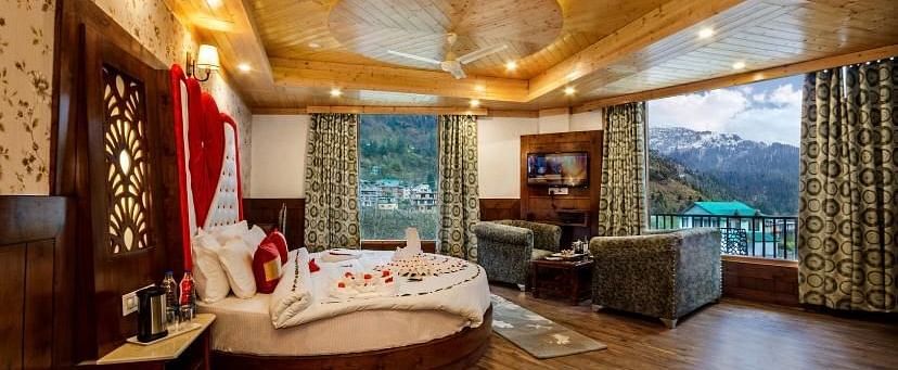 A spacious and luxurious hotel room with a round bed, plush seating, a balcony overlooking a scenic view, and elegant decor | DLS La Serene Manali
