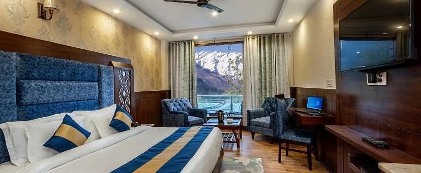  A spacious hotel room with a comfortable bed, a seating area, and a view of mountains | DLS La Serene Manali