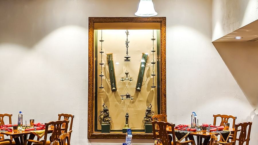 Traditional restaurant setting featuring wooden tables set with red napkins and water bottles, under a rustic chandelier, with a framed display of cultural artifacts on the wall.