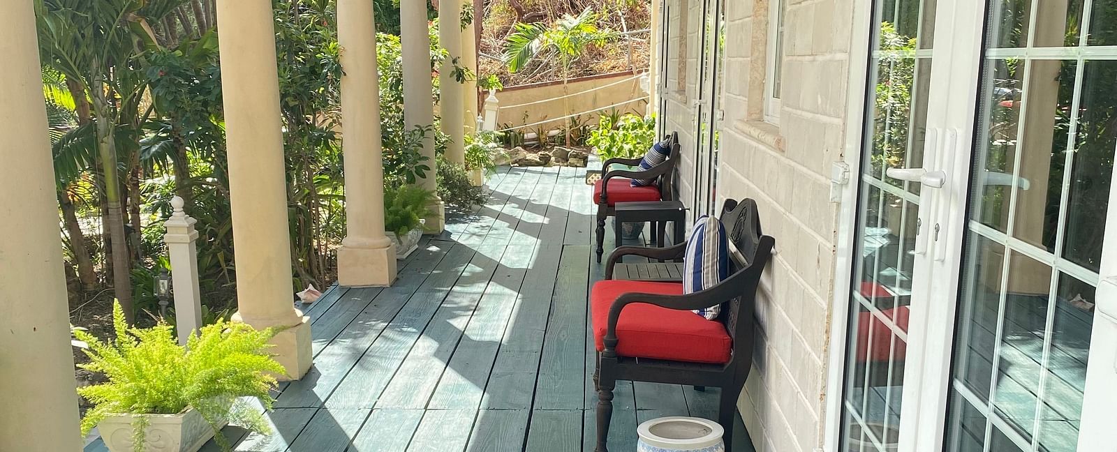 Outdoor walkway with green wooden flooring and red chairs outside a room | A Stone's Throw Away