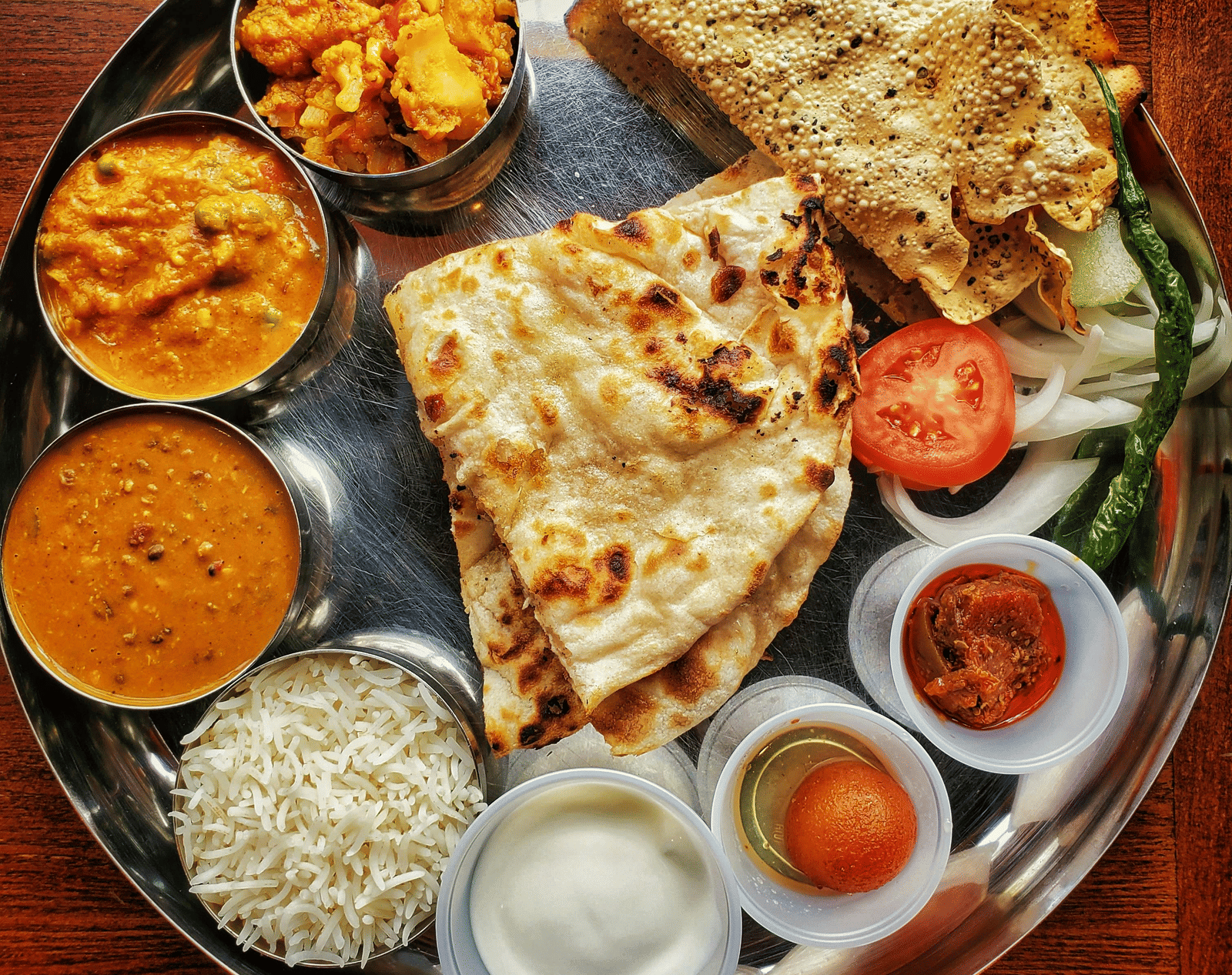 A neatly arranged plate with several Indian delicacies served.