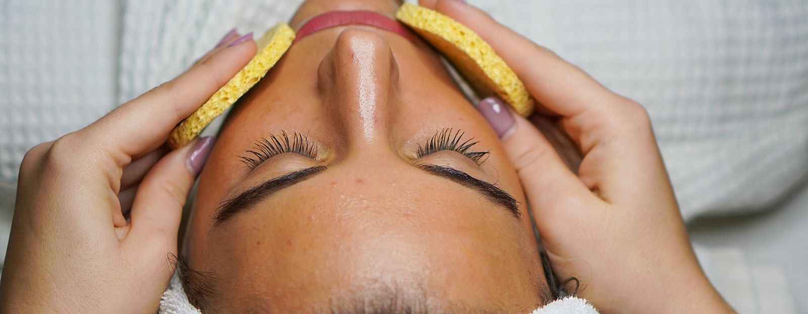 Image of a woman with towel wrapped around her hair getting a facail.