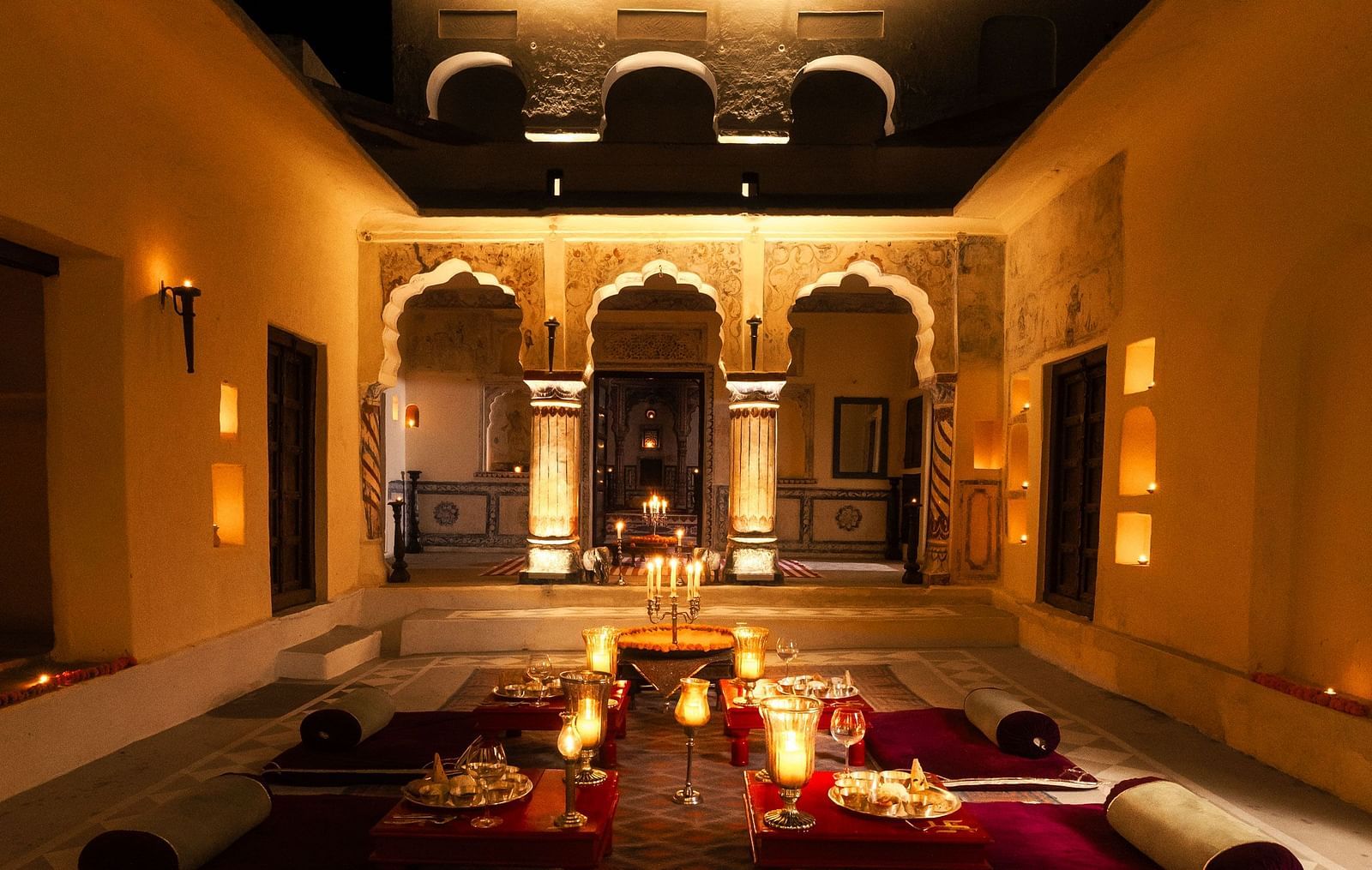 A softly lit courtyard at Fort Barli, with arched doorways and floor seating, creates a magical evening ambience.