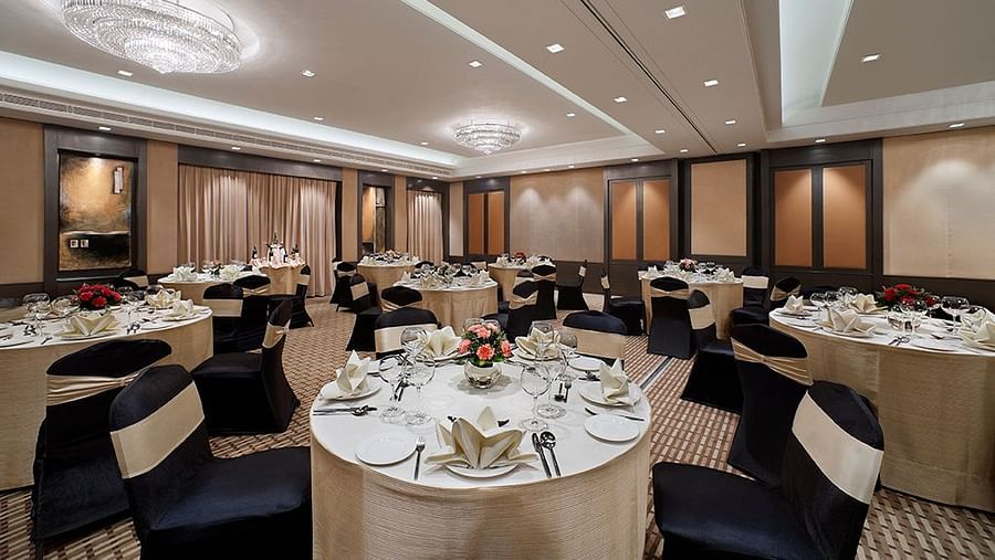 Banquet hall with round tables set for a formal event, featuring chandeliers and high ceilings.