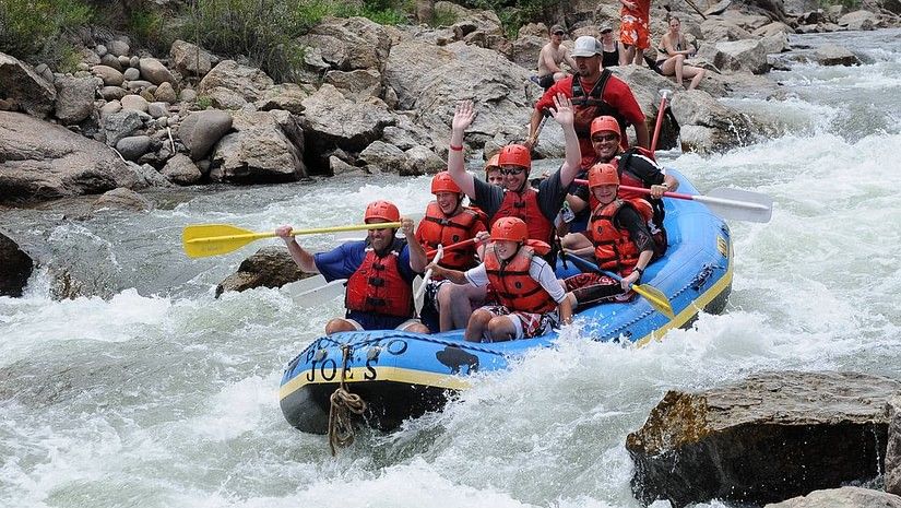 Group white water rafting on a rough river wearing red life jackets.