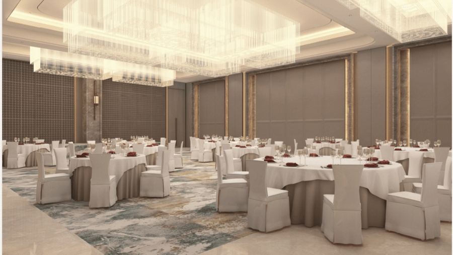Banquet hall at Tulip Inn Bidar set up with 9 round dining tables, chairs with fabric covers, chandelier light fixtures, and patterned carpet.