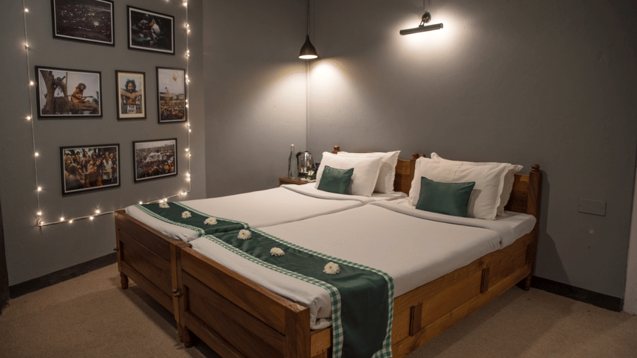 A hotel bedroom with twin wooden beds, white linens, matching runners, framed photo wall, and warm ambient lighting.