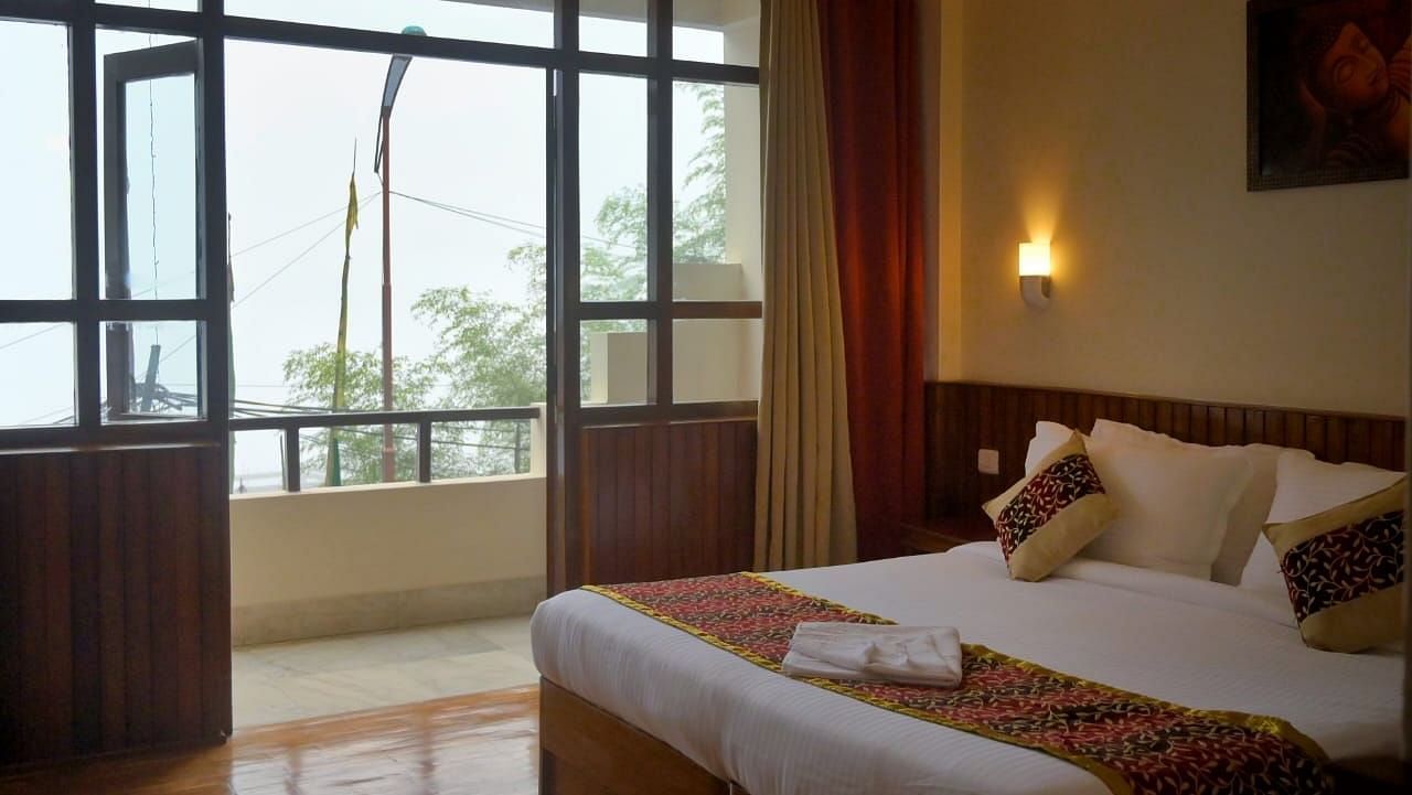 An image of the super deluxe room at Ecotel Chiminda, Pelling featuring a queen size bed, and an expansive door leading to the balcony