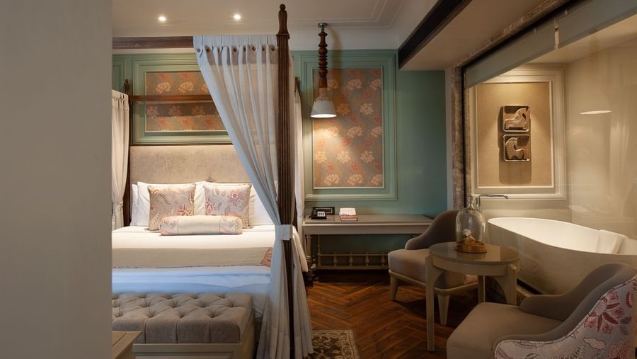 A serene corner of a suite at The Evren, Vagator, showing the four-poster bed and a glimpse of the luxurious bathroom with a freestanding bathtub visible through a glass partition.