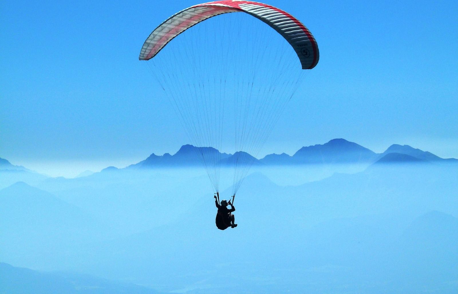 A person soaring through the sky while paragliding, experiencing the thrill of flight against a clear blue backdrop.