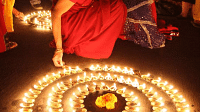 A person in a red outfit kneels to arrange lit candles in a large circular pattern on the ground.