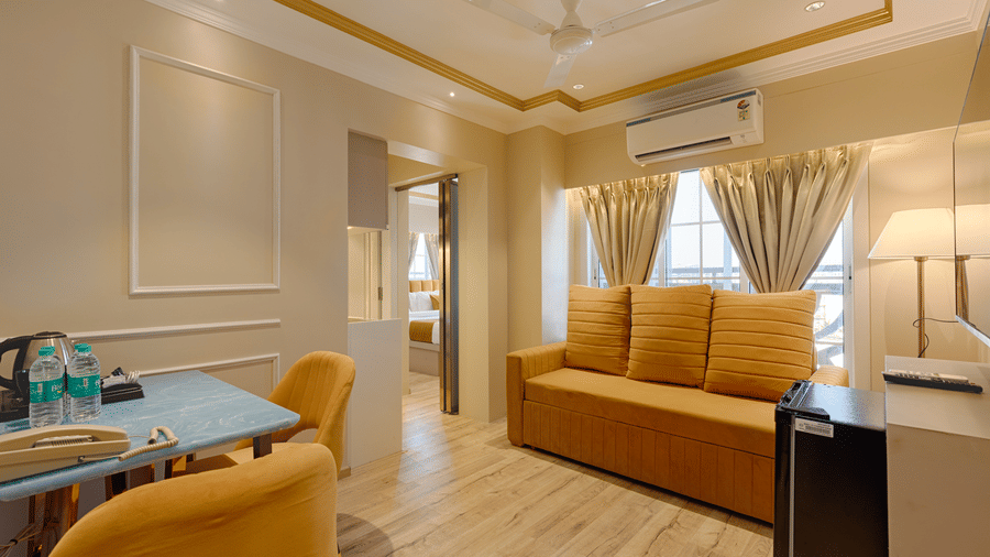 A bright living area in a suite featuring a yellow sofa, dining table, and air conditioning - Home2 Residency, Mumbai Airport