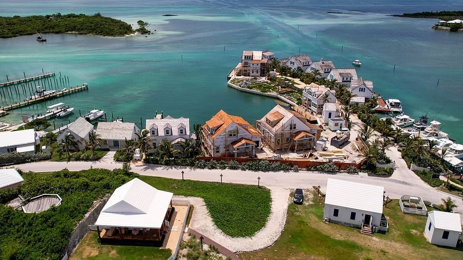 Aerial shot of a coastal resort with clustered villas, green landscaping, and a winding waterfront promenade | Abaco Inn
