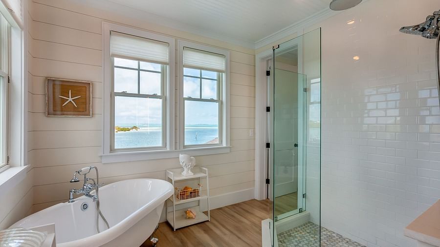 a bathroom with a bathtub, wooden floor, walk in shower, and windows that overlooks the sea at Abaco Inn.