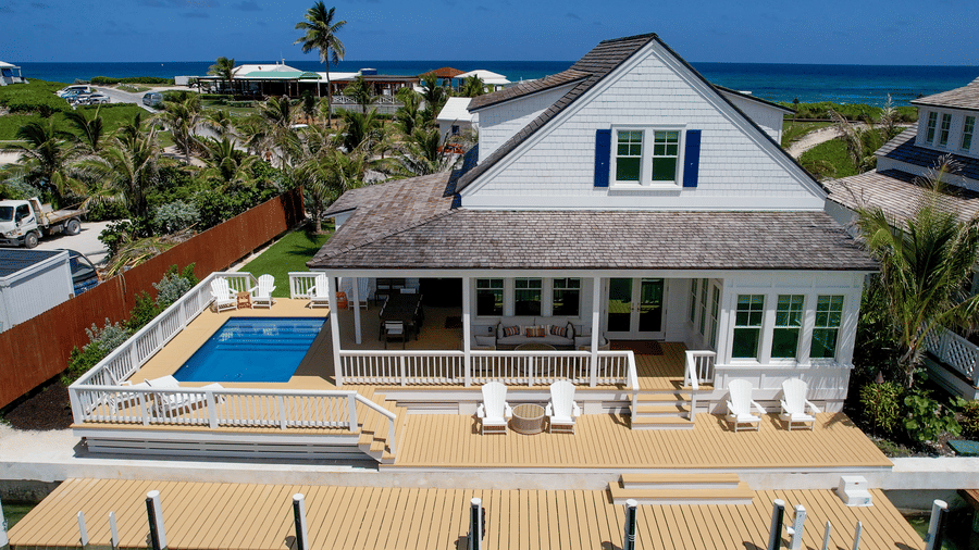 An exterior view of a waterfront villa with a wooden deck, outdoor seating, and the ocean visible behind at Shoal Villa in Abaco Inn.