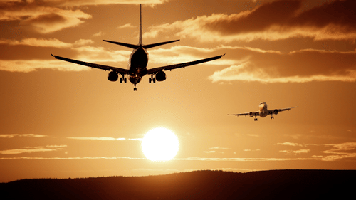 Two planes flying with a sunset and clouds in the background
