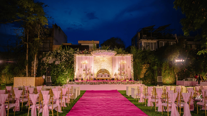 The Brij Nest Lawn featuring a floral stage, aisle seating, ambient lighting, and landscaped surroundings prepared for an evening celebration | Clarks Amer, Jaipur