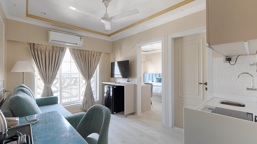 A multi-functional living space with a teal sofa, dining chairs, and a visible kitchenette - Home2 Residency, Mumbai Airport