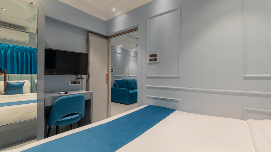 View of a bedroom showing a wall-mounted TV and a large mirror reflecting the blue-accented bed - Home2 Residency, Mumbai Airport